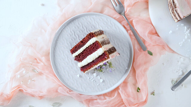 Overhead view of red velvet cake slice with cream layers on a plate over pink fabric