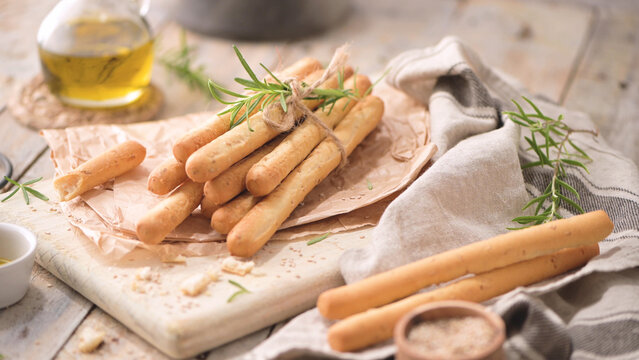 Crispy Italian breadsticks tied with fresh rosemary on a rustic wooden board