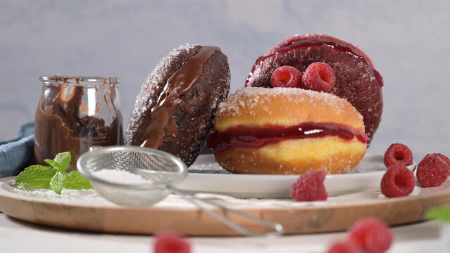 Assorted sweet donuts filled with jam and chocolate served with fresh raspberries and a jar of spread
