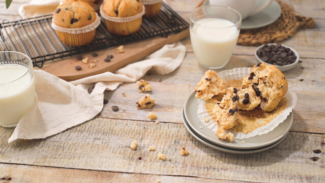 Freshly baked chocolate chip muffins with glasses of milk on a rustic wooden table