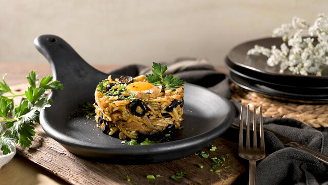 Gourmet rice dish with black olives and a fried egg served in a black pan