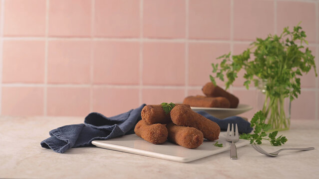 Golden fried croquettes served on a white plate with fresh parsley and a blue cloth against pink tiles