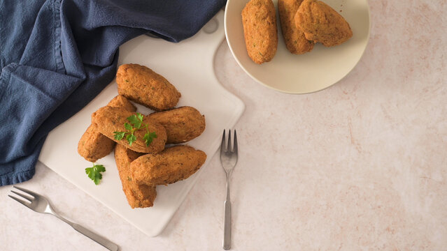 Golden fried croquettes with parsley on a white board and plate