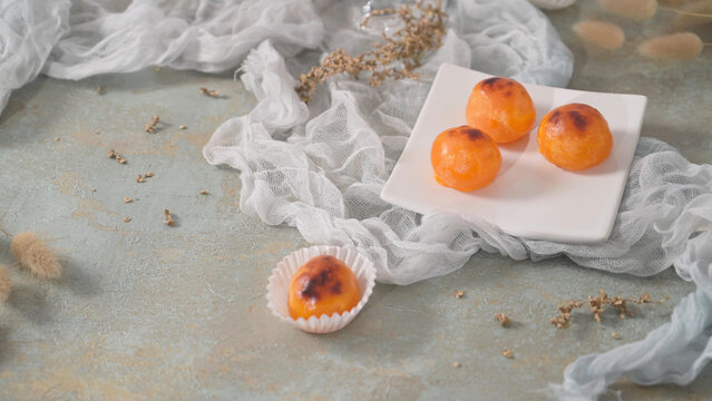 Sweet glazed orange egg pastries styled on a white plate with rustic gauze fabric