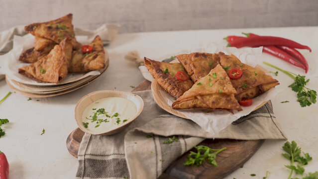 Crispy golden samosas served with dipping sauce and fresh chili on a wooden board