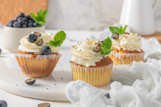Three frosted cupcakes with blueberries and mint on a white marble board