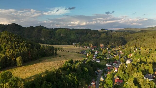 Aerial view of village nestled in forested valley among sandstone hills at golden hour in Bohemia, Czech Republic