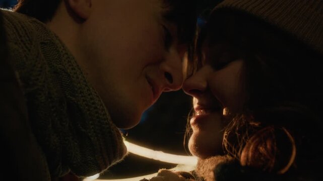 Young Caucasian couple smiling and leaning heads together outdoors at night during winter. Footage is ideal for holiday marketing campaigns and romantic relationship advertisements