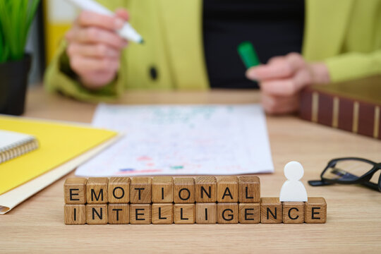 A person engages in a creative activity at a desk, focusing on emotional intelligence. Wooden letters spell it out, while colorful notes and a plant add an inspiring touch to the scene.