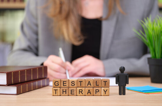 In a cozy therapy setting, a professional is engaged in writing notes while gestalt therapy blocks are arranged on the table. A small figure represents the client, emphasizing personal growth.