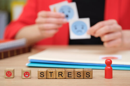In a calm workspace, a person holds images depicting various emotions while wooden blocks spell out stress. This scene highlights a creative approach to understanding feelings.