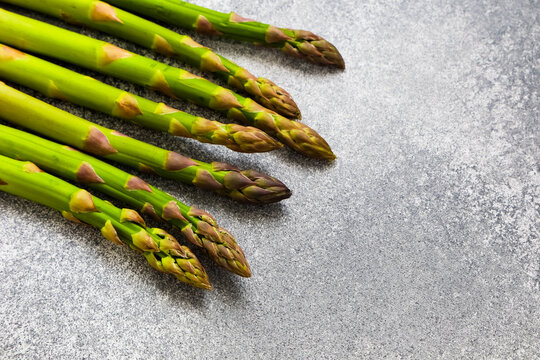 Fresh asparagus arranged on a gray surface with natural light shining on the tips