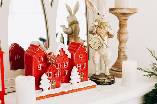 Decorative Christmas red houses and a clock-wearing rabbit on a mantel during a winter celebration