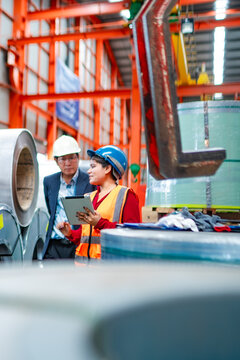 Factory manager and female engineer reviewing steel coil inventory with tablet in warehouse, checking material stock, manufacturing operations and production management.