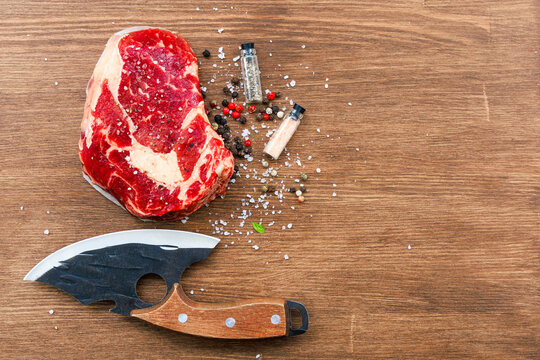 Fresh cut of beef on wooden surface with spices and a knife nearby