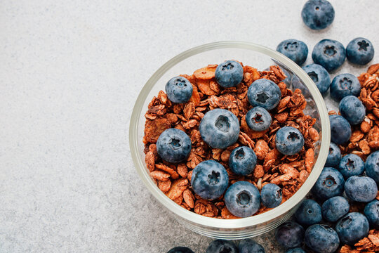 Bowl of granola with blueberries placed on a gray surface in a kitchen setting