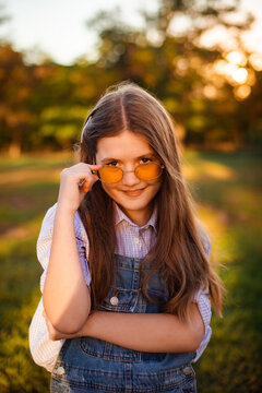 playful young girl lowering yellow sunglasses with sly smile in park