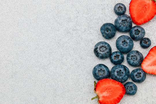 Fresh strawberries and blueberries placed on a gray background during daytime