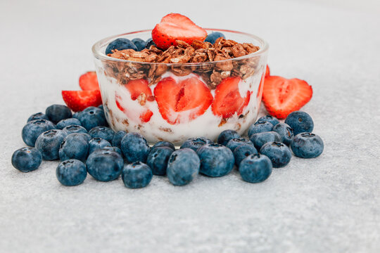 Bowl of yogurt with granola and fresh fruit on a light gray surface