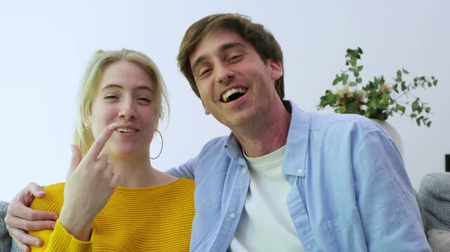 A happy young couple is seen smiling and laughing while talking and waving at the camera during a friendly video call or online chat from their home.