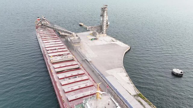 An aerial drone shot flies forward and pans down over the bulk carrier CSL Tadoussac, capturing its red cargo deck and forward bridge while docked at an industrial pier