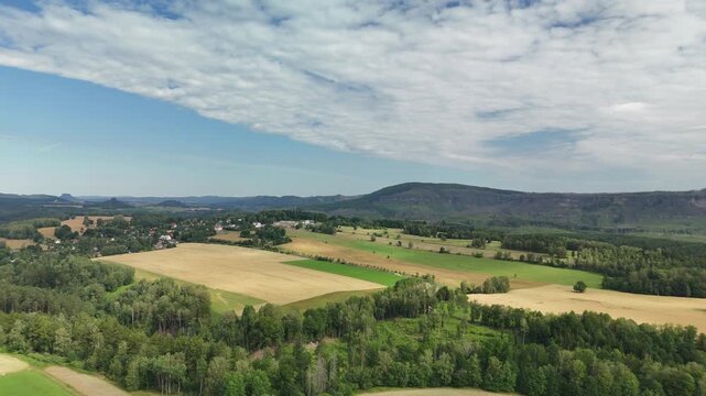 Aerial drone view of golden grain fields and green meadows below a flat topped wooded ridge