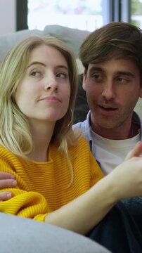 A young couple shares a relaxed moment on the sofa, talking and interacting with a digital device together.