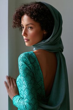 Contemplative portrait of woman in emerald lace dress and headscarf by window for fashion editorial poster and magazine layout