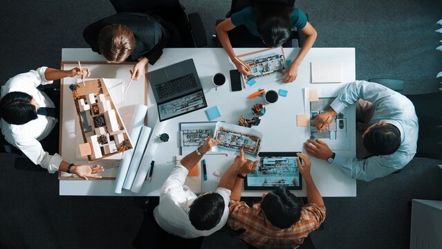 Architect team discussing and pointing and presenting blueprint to interior designer. Aerial view professional business people brainstorming building interior at table with house model. Alimentation.