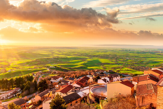 scenic evening sunset landscape with beautiful view og vintage town with traditional roofs and houses and green and golden walley hills with farmland and cloudy sky