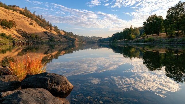 Golden hills and trees border a still river reflecting a sky