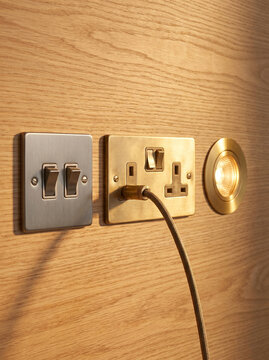 Modern Interior Wall Fixtures Showing Stainless Steel Light Switches Brass Socket Outlet with Plug and Warm LED Downlight Recessed in Oak Panel