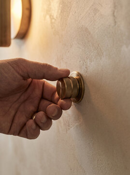 Extreme Close-Up View of Electrician Hand Fine-Tuning Antique Brass Knurled Rotary Dimmer Switch Control Knob on Warm Plastered Wall Surface