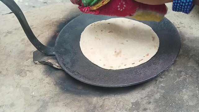 Woman hands pressing and cooking traditional Indian flatbread roti on hot iron tawa