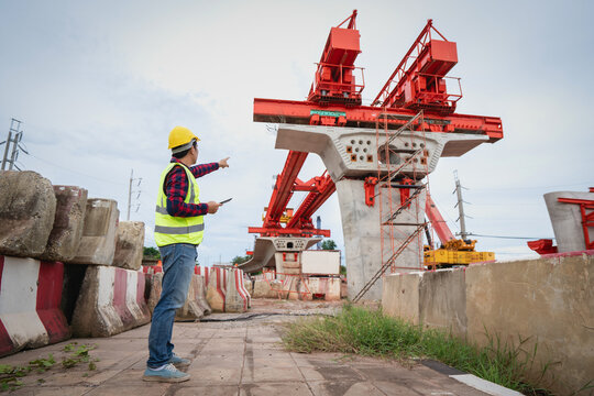 Asian foreman is writing a work summary on a tablet, digitizing the information before leaving work on a construction site for a new concrete road and bridge a critical infrastructure project.