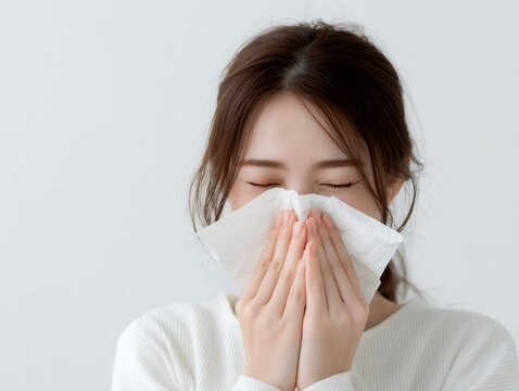 ティッシュペーパーで鼻をかむ花粉症や風邪の症状に悩む白い服を着た茶髪の若い女性
