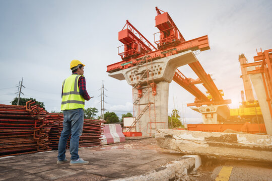 Asian civil engineers use tablets to record electronic data at a concrete highway bridge construction site. A male supervisor is inspecting things at the new concrete road and bridge construction site