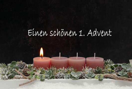 Einen sch&ouml;nen 1. Advent &ndash; Grusskarte mit einer brennenden altrosa Kerzen auf modernem Adventsgesteck vor dunklem Hintergrund.