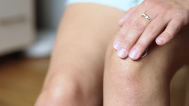 Woman applies soothing cream to knee injured after electric scooter fall. She gently treats swelling while recovering from painful trauma.