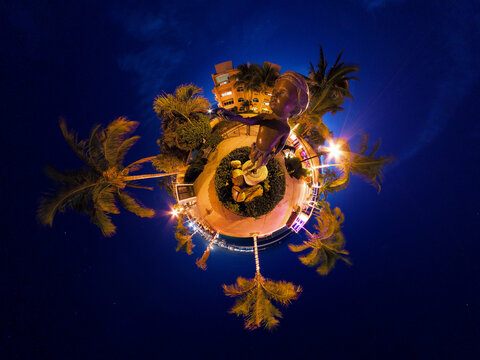 View of the Malecon de La Paz at night in a 360-degree little planet projection, featuring palm trees, street lights, and the Pearl Diver statue in La Paz, Baja California Sur, Mexico.