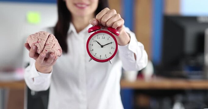 In a lively office, a woman showcases her unique approach to productivity, holding a brain model in one hand and a ticking clock in the other, merging creativity and time management.