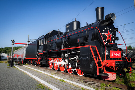 View of a vintage black steam locomotive with red wheels and a prominent red star on the front, parked on railway tracks in Solovetsky, Arkhangelsk Oblast, Russia.
