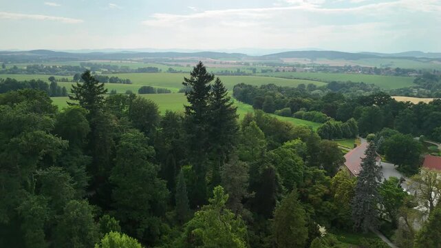 Drone shot of the Arboretum Wojsławice treetops with buildings and farmland stretching to the horizon in summer in Poland