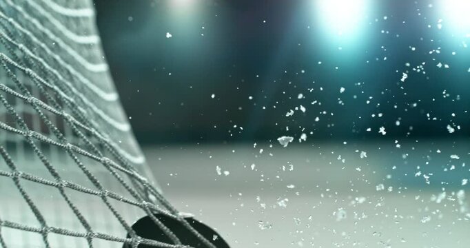 Extreme super slow motion close-up of an ice hockey puck striking the goal net at 1000 fps, with ice particles exploding on impact and a blurred winter stadium and rink in the background.