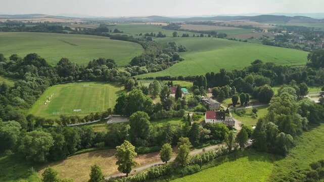 Aerial view of green countryside with fields trees and a village below forested hills in Poland in summer