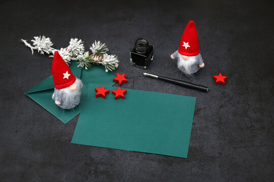 Blank Christmas greeting card with space for text. Dark green card with envelope, cute gnomes, a dip pen, and red stars against a dark background.