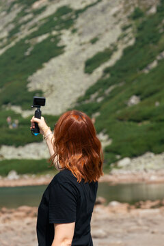 woman recording video holding action camera standing at high tatras lomnicky stit lake shore wearing black t shirt outdoor nature landscape concept of travel adventure tourism recreation lifestyle