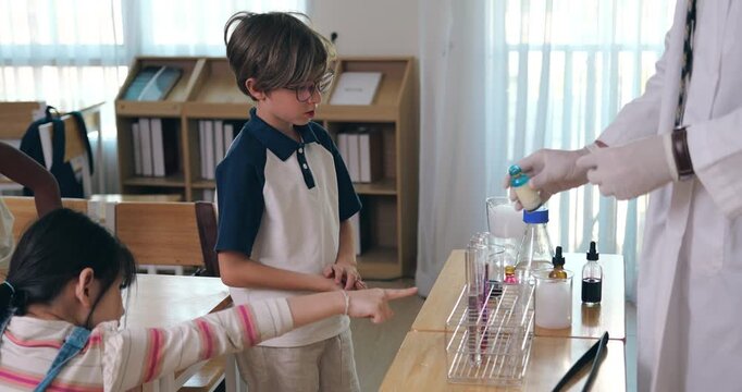 Young boy with glasses participating in fun chemistry experiment with teacher holding test tube in classroom.