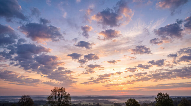 Vivid sunset sky with spectacular, dramatic clouds over a panoramic landscape of misty rolling hills and trees.
