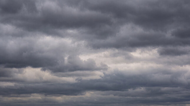 Heavy, dramatic dark grey storm clouds gather across a vast sky, foreshadowing impending bad weather and rain.